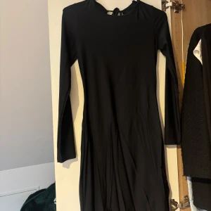 Svart långärmad klänning med öppen rygg - Elegant svart klänning med långärmade och en  öppen rygg. Perfekt för alla tillfällen!! Klänningen har en knytning i ryggen för extra detalj och slits vid låret. Endast använd 1 gång (behöver strykas) Har en exakt samma i Xs då jag beställde två storlekar och säljer båda så det är bara att höra av sig vid intresse❤️❤️