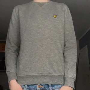 Grå sweatshirt från Lyle & Scott - Säljer en grå sweatshirt från Lyle & Scott i storlek M, skulle tippa på att det är JR storlek eller att den krympt. Sitter som XS, passade mig då jag var runt 160-165. Lite skrynklig då den legat i garderoben över 2 år snart, men det går lätt fixa till! Finns ett litet hål i vänster ärm som syns på bild 3. Bara att höra av sig vid frågor!