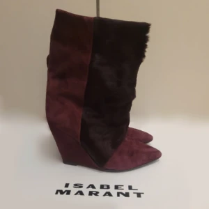 Vinröda boots från Isabel Marant - Snygga vinröda boots från Isabel Marant i mocka och päls. De har en spetsig tå och kilklack, vilket ger en elegant look. SNYGGASTE skorna jag sett men är tyvärr lite för små för mig som vanligtvis har 38-37!! 36 men passar nog även 37❤️ SÅ så sjukt snygga och trendiga!!!! Samma finns på VC för 14000!!!! Sparsamt använda så i toppskick! Nya sulor är även påsatta av skomakare ❤️❤️ kom med prisförslag men säljer endast till bra pris!! !äkta läder och päls! 