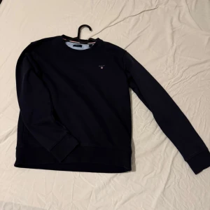 Marinblå sweatshirt från Gant - Säljer en stilren marin sweatshirt från Gant. Tröjan har långa ärmar och en liten broderad logga på bröstet. Perfekt för en avslappnad och snygg look. Storlek S passar på xs också, pris kan diskuteras