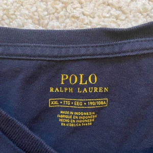 Mörkblå t-shirt från Ralph Lauren - Säljer en klassisk mörkblå t-shirt från Ralph Lauren med den ikoniska röda loggan broderad på bröstet. T-shirten är kortärmad och tillverkad i mjuk bomull. Perfekt för en avslappnad stil.