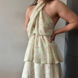 Blommig klänning från Gina Tricot - Säljer en söt blommig klänning från Gina Tricot. Den har en halterneck-design med öppen rygg och volanger. Perfekt för sommarens varma dagar. Klänningen är i en ljus färgton med blommönster i rosa och grönt💗