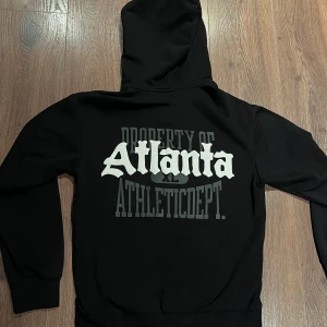 Svart zip hoodie  - Snygg svart hoodie med dragkedja och tryck av 'Atlanta' på bröstet och ryggen. Perfekt för en avslappnad stil.