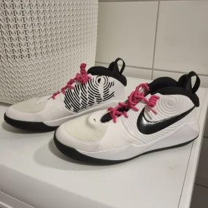 Vita och svarta Nike sneakers med rosa snörning - Snygga vita och svarta Nike sneakers med rosa snörning och svart Nike-logga. Skorna har en unik design med cirkulära mönster på sidorna och en bekväm passform. Perfekta för en sportig look.
