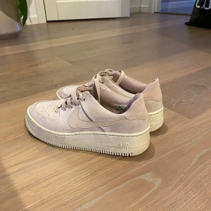 Nike Air Force i ljusrosa mocka - Säljer ett par ljusrosa Nike Air Force sneakers i mocka. Skorna har en klassisk design med snörning och en robust sula. Perfekta för en stilren look.