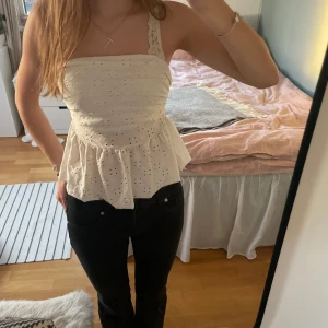 Vit axelbandslös topp med spetsdetaljer - Säljer en söt vit axelbandslös topp med spetsdetaljer och volang nedtill. Perfekt för sommardagar och kan enkelt matchas med en kofta eller jacka. Säljer även koftan