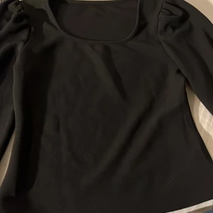 Svart långärmad topp - Snygg svart långärmad topp med rund halsringning. Perfekt för en stilren look. Materialet ser mjukt och bekvämt ut, vilket gör den idealisk för både vardag och speciella tillfällen.