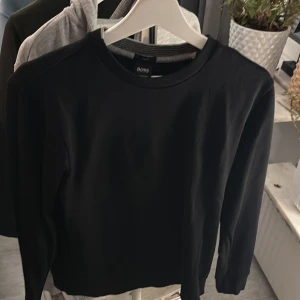 Svart tröja från Boss - Säljer en stilren svart tröja från Boss. Tröjan har en klassisk design med rund hals och långa ärmar. Perfekt för en minimalistisk look.