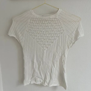 Vit stickad topp - Säljer en vit stickad topp med korta ärmar och ett snyggt hålmönster framtill. Perfekt för en stilren och luftig look. Passar bra till både jeans och kjol. Hör av dig vid intresse!