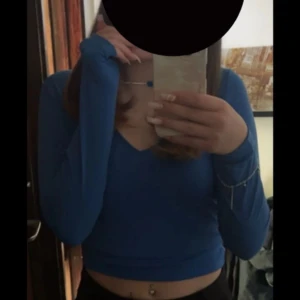 Blå långärmad topp från Bikbok  - Snygg blå långärmad topp från bikbok  med v-ringning med en perlad ”kedja” Perfekt för en stilren look. Toppen är croppad och har en figurnära passform.