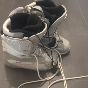 Grå snowboard boots från Crazy Creek - Säljer ett par grå snowboard boots från Crazy Creek. De har snörning och en robust design som passar perfekt för vintersport. Bootsens insida är vadderad för extra komfort och värme.