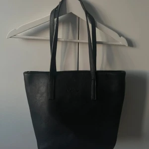 Svart axelväska med dragkedja - Snygg svart axelväska i syntetmaterial med praktisk dragkedja på baksidan. Väskan har långa handtag och rymligt inre med flera fack för enkel organisering. Perfekt för att bära med sig allt man behöver under dagen. Från hm