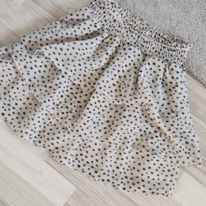 Beige prickig kjol med volanger - Charmig beige kjol med svarta prickar och volanger. Den har en elastisk midja för bekväm passform. 💕