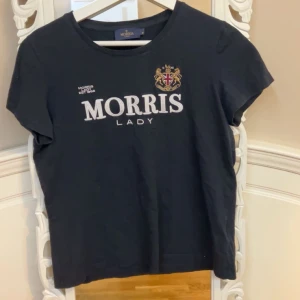 Svart t-shirt från Morris - Snygg svart t-shirt från Morris med broderad logga och texten 'Morris Lady' på framsidan. Perfekt för en stilren look med en touch av elegans. T-shirten har korta ärmar och rund halsringning.