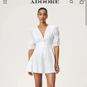 Vit klänning från ADOORE - Säljer en söt vit klänning från ADOORE med puffiga trekvartsärmar och v-ringning. Klänningen har blommönster och en markerad midja. Perfekt till studenten eller midsommar. Storlek s.