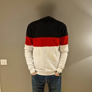 Svart, röd och vit tröja från Guess - Säljer en snygg tröja från Guess i svart, rött och vitt. Tröjan har en broderad logga på bröstet och långa ärmar. Storlek är XS mdn är stor för storleken. Jag själv är S/M men den sitter bra på mig. Vid funderingar är det bara att skriva// Merch Åled