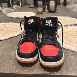 Nike Air Jordans i svart, röd och vit - Snygga Nike Air Jordans i klassisk färgkombination av svart, röd och vit. Skorna har hög snörning och den ikoniska Nike-loggan på sidan. Perfekta för dig som vill ha en stilren och sportig look.