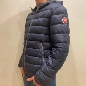 Colmar jacka - En marinblå dunjacka från colmar. Jackan är i bra skick. Den har en defekt på högra axeln som man kan se på andra bilden. Hålet är lagat med en liknande tygbit så att det ska synas så lite som möjligt. Därför är priset så lågt. Priset kan diskuteras. Storleken är 48 vilken innebär S
