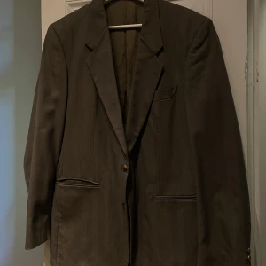 Brun kavaj från Drabant Sweden - Elegant brun kavaj från Drabant Sweden med klassisk design. Kavajen har två knappar framtill och fickor med lock. Perfekt för en stilren look.