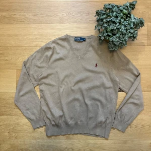 Beige tröja från Polo Ralph Lauren - Säljer en stilren beige tröja från Polo Ralph Lauren med det klassiska broderade logotypen i rött på bröstet. Tröjan har en v-ringad hals och långa ärmar, perfekt för en elegant old money look. Den är i jättefint skick och jag säljer den för bara 299kr då nypris på denna ligger på ungefär 2200kr. Hör gärna av dig om du har några frågor!