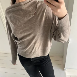 COS Beige tröja med unik krage - Säljer en stilren beige tröja med en unik krage som kan bäras på olika sätt. Tröjan har långa ärmar och en mjuk, bekväm passform. Perfekt för en avslappnad look.