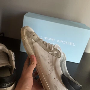 Vita sneakers från Philippe Model - Snygga vita sneakers från Philippe Model med svarta detaljer och snörning. Skorna har en stilren design med en kontrasterande svart häl och en bekväm passform. Storlek 46 passar även 45. Synliga deffekter. Perfekt för våren. Priset kan diskuteras vid snabb affär 