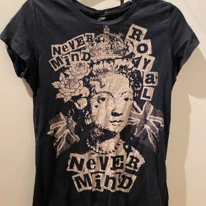Svart t-shirt med tryck från Gina Tricot - Cool svart t-shirt från Gina Tricot med ett unikt tryck av en kunglig figur och texten 'Never Mind Royal'. Perfekt för en avslappnad stil med en twist. Kortärmad och i mjukt material.