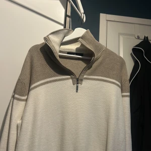 Beige och vit tröja från Park Lane - Säljer en stilren beige och vit tröja från Park Lane. Tröjan har en dragkedja vid halsen och en ribbad krage. Perfekt för en avslappnad och snygg look.