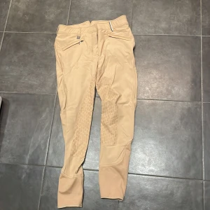 Beige ridbyxor från JH Collection -  Säljer ett par snygga beige ridbyxor från JH Collection med dragkedja och stilrena detaljer. Byxorna har en tight passform och är perfekta för ridning. De är designade med en hög midja och har förstärkningar på insidan av benen för extra hållbarhet.