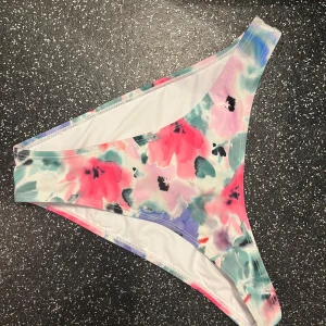 Blommig bikiniunderdel - Snygg bikiniunderdel med ett färgglatt blommönster i rosa, blått och grönt. Perfekt för sommaren. Tillverkad i ett mjukt och bekvämt material som sitter bra på kroppen. Ej testad! Kan mötas upp vid önskemål :) 