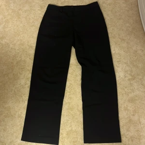 Svarta kostymbyxor från Gina Tricot - Snygga svarta byxor från Gina Tricot i storlek 38. De har en klassisk design med rak passform och är perfekta för en stilren look. Byxorna är tillverkade i ett bekvämt material som passar till många olika tillfällen.