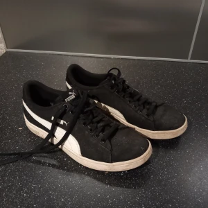 Svarta sneakers från Puma - Snygga svarta sneakers från Puma med vita detaljer och snörning. Skorna har en klassisk design med Pumas logga på sidan och hälen. Sparsamt använda, Tvättar dem såklart innan fraktning. 