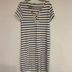 Randig klänning med snörning - Snygg och bekväm randig klänning i vitt och svart med korta ärmar. Den har en cool snörning framtill som ger en extra detalj. Perfekt för en avslappnad stil.