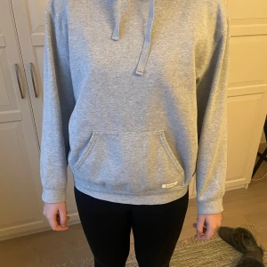 Grå hoodie från Björn Borg - Säljer en stilren grå hoodie från Björn Borg i storlek M men skulle säga att den är liten i storleken och passar s-xs. Den har en klassisk design med en stor ficka framtill och justerbar huva. 