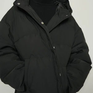 Svart pufferjacka med huva - Snygg svart pufferjacka med huva och dragkedja. Jackan har en oversized passform och långa ärmar, perfekt för kyliga dagar. Den är använd för två år sen på vintern men inte mer än det! Super fin! Kan skicka egens bilder:)