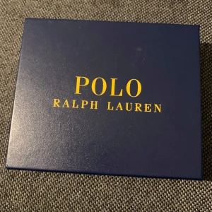 Brun plånbok från Polo Ralph Lauren - Helt oanvänd och inga tecken på användning brun plånbok i skinn från Polo Ralph Lauren. Den har flera kortfack och en myntficka, perfekt för att hålla ordning på dina tillhörigheter. Diskret logotyp präglad på framsidan. 