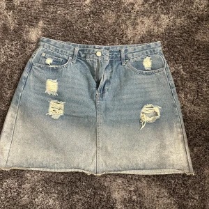 Blå jeanskjol från Ally - Snygg blå jeanskjol från Ally med slitna detaljer och femficksdesign. Kjolen har en knapp och dragkedja framtill och är perfekt för en avslappnad stil.