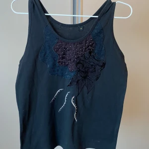 Svart topp/linne med vintage detaljer - Svart topp/ linne med coola detaljer och broderingar. Toppen är köpt second hand och ser ut som ny. Måtten står på bilden men för att förtydliga: Bild 3 från sida till sida rakt över: 44cm. Bild 4 uppifrån och ner som visas på bilden: 48cm. Skriv gärna om funderingar uppstår/ behöver mer bilder eller mått❣️