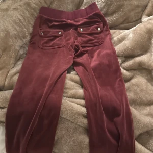 Vinröda byxor med fickdetaljer - Snygga vinröda byxor i mjukt material med fickor och knappar bak. Perfekta för en avslappnad stil. Köpt på juicy contoure. Använt dom ungefär tre gånger bara