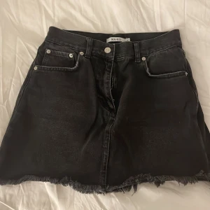 Svart jeanskjol från NA-KD - Snygg svart jeanskjol från NA-KD med fransig kant och klassisk femficksdesign. Perfekt för en avslappnad stil. Kjolen har en knapp och dragkedja framtill❤️