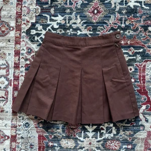 Brun mini kjol! - Brun mini kjol med veckad design. Kjolen har en knapp och dragkedja i sidan för enkel på- och avtagning. Perfekt för en stilren look. Endast testad, köpt för några år sedan, men i superbra skick! 