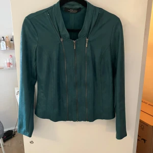 Grön jacka från One Two Luxzuz - Snygg grön jacka från One Two Luxzuz i microfiber polyester och elastan. Jackan har en stilren design med dragkedja framtill och långa ärmar. Perfekt för en chic look.