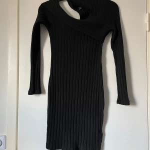 Svart ribbad klänning - Snygg svart ribbad klänning med lång ärm och unik omlott-design vid halsen. Perfekt för en stilren look.
