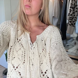 Beige stickad tröja med snörning - Säljer en mysig beige stickad tröja med snygg snörning framtill. Tröjan har en avslappnad passform och långa ärmar, perfekt för kyligare dagar. Den har ett vackert stickat mönster som ger en unik touch.