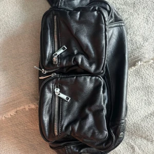 Svart axelväska noella - Snygg svart axelväska med flera praktiska dragkedjor och nitar på axelremmen