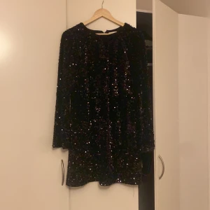 Svart glittrig klänning från H&M - Snygg svart klänning från H&M med glittriga paljetter som täcker hela plagget. Klänningen har långa ärmar och en kort längd, perfekt för en festlig kväll. Den har en dragkedja på sidan för enkel på- och avtagning.