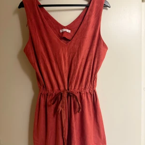 Röd byxdress från Mango - Snygg röd klänning från Mango med v-ringning och knytband i midjan. Perfekt för en avslappnad stil. Tillverkad i ett mjukt material som ger en bekväm passform.