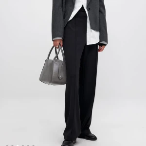 Svarta kostymbyxor - Eleganta svarta kostymbyxor med hög midja och vida ben. Perfekta för en stilren look. Byxorna har en klassisk design med dragkedja och knappar framtill. Använda ett fåtal gånger! Nypris 499!