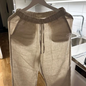 Beige linnebyxor med snörning - Snygga och bekväma beige linnebyxor med elastisk midja och snörning. Perfekta för en avslappnad stil. Byxorna har en loose passform och är idealiska för varma dagar.