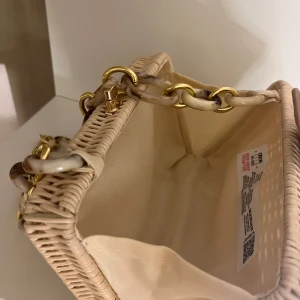 Beige strandväska med kedjedetaljer - Snygg beige korgväska med en unik kedja i plast och metall, från ASOS. Väskan har en stilren design med en praktisk stängning upptill. Perfekt för sommaren! 